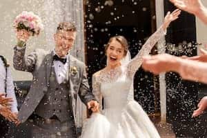 happy bride and groom leaving church while guests throw birdseed