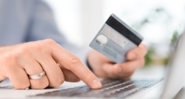 hand holding credit card and other hand typing on computer